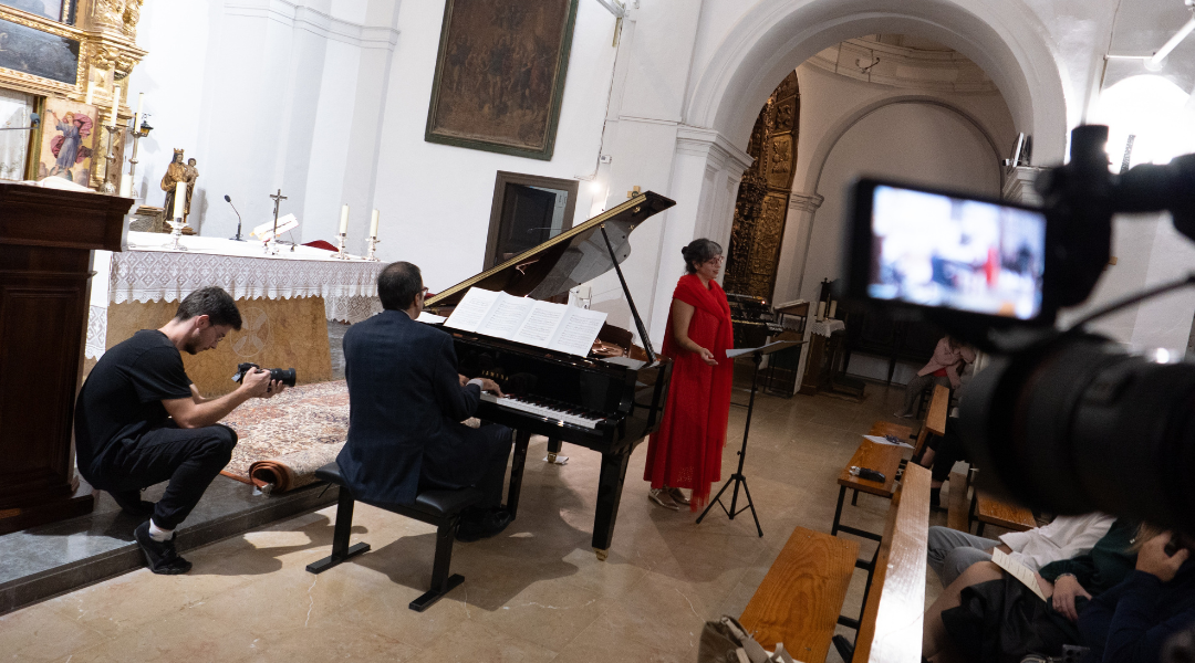 Concierto piano y voz – Proyecto Raíces Vivas ✅ Leyenda Actuación musical con piano y voz en una iglesia, mientras un cámara graba la actuación.