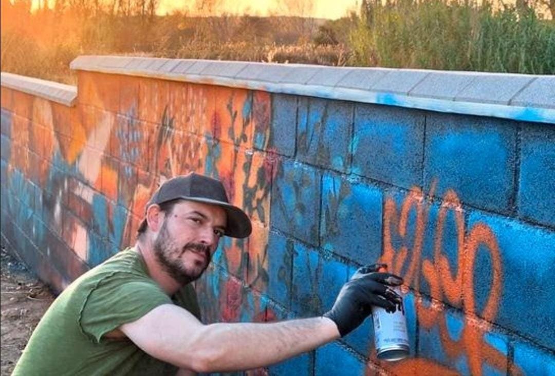 Artista pintando un mural con spray durante un evento cultural de Va de Arte al atardecer