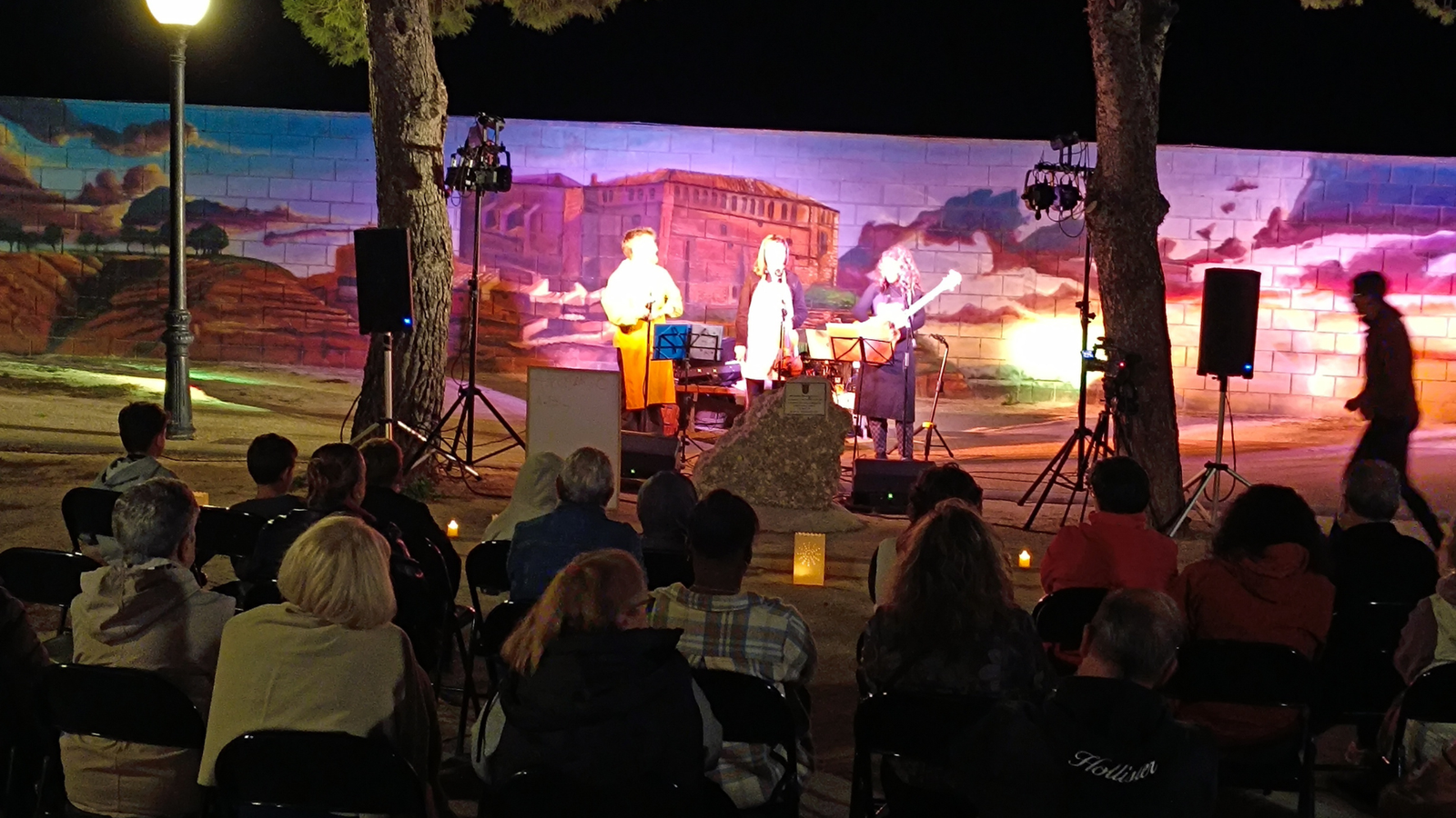 Concierto nocturno de Va de Arte con público al aire libre en Zuera frente a un mural iluminado